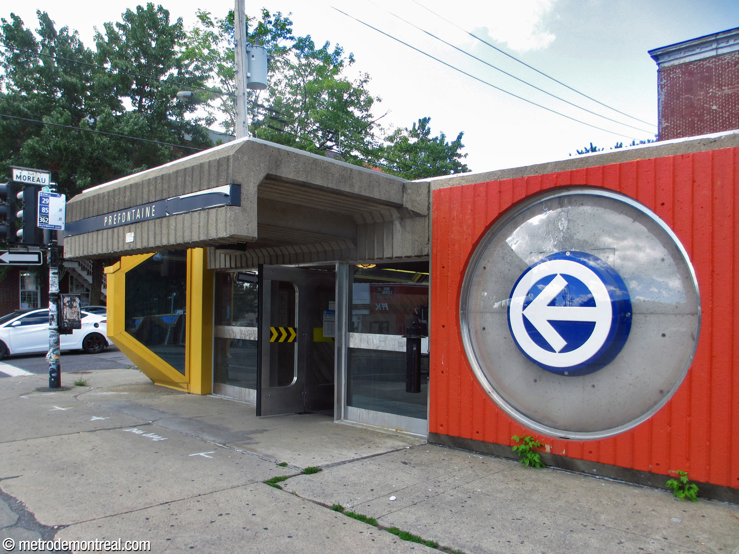 Entrée avant de l'édicule nord. On remarque l'imposant auvent en béton et un logo de métro décoratif sous une bulle en plastique; la flèche du logo pointe les portes d'entrée.