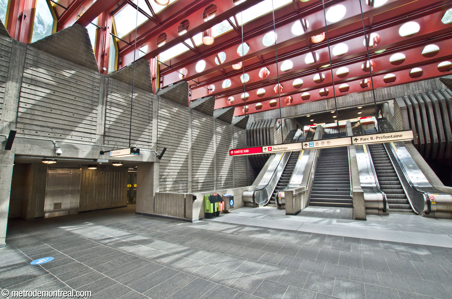 La large volée d'escaliers fixes et mécaniques entre la mezzanine et la sortie Hochelaga Sud. À côté, une double travée en retrait donne accès à l'ascenseur vers la surface.