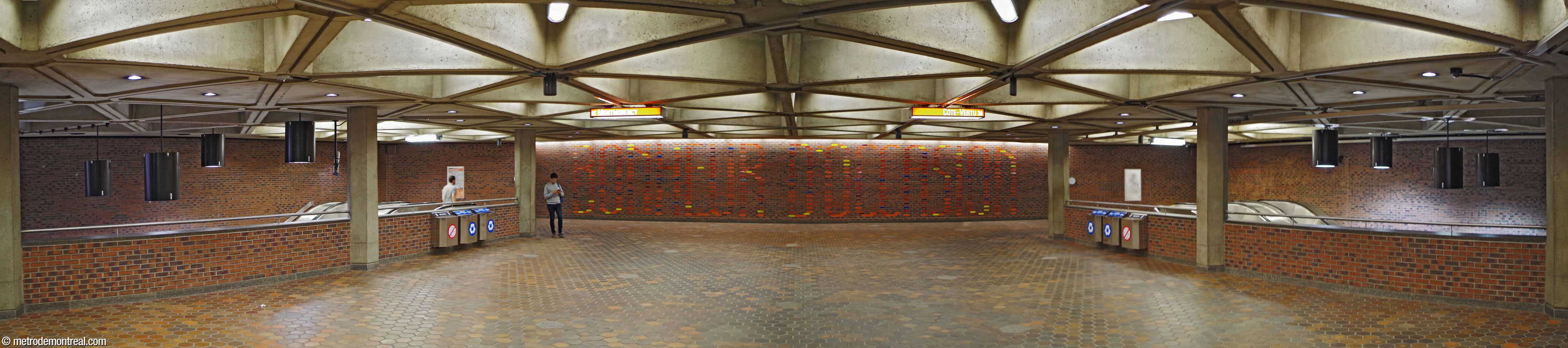 The broad fare-paid zone at the western end of the concourse, leading to the stairwells to the Montmorency (left) and Côte-Vertu (right) platforms. Julien Hébert's mural Bonheur d'Occasion occupies the back wall.