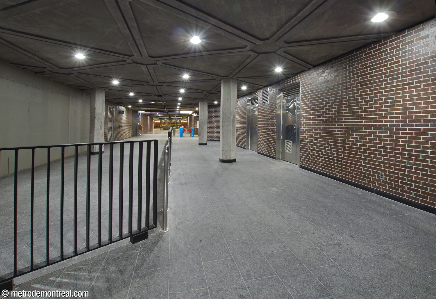 The hallway connecting the station to the two eastern headhouses, looking back toward the ticket hall. The hallway is divided into a fare-free zone at left, and the fare-paid zone connecting the station’s two elevators at right.