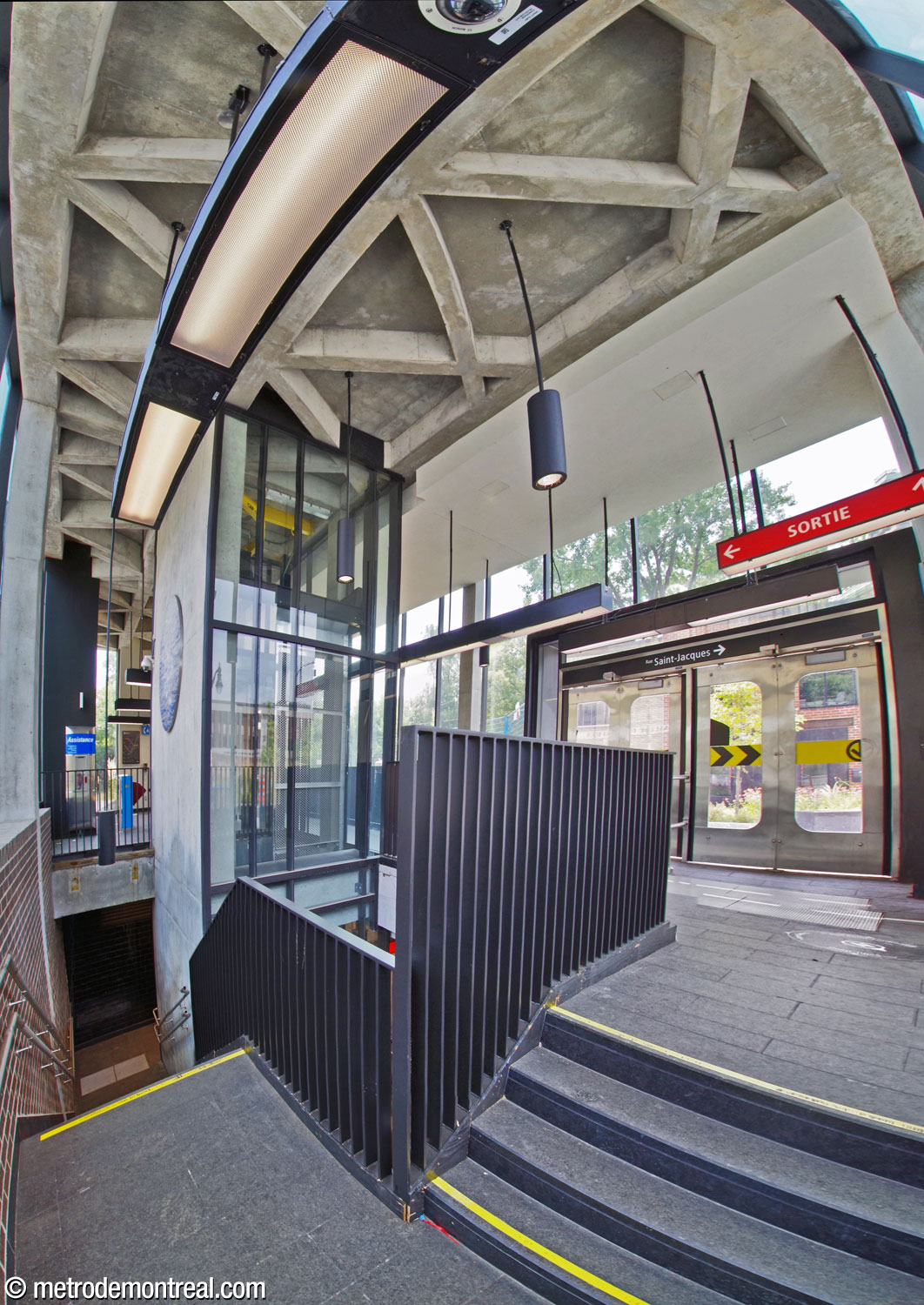 The interior of the Place Saint-Henri headhouse from the northeast corner, at the upper landing of the north stairwell. At left, the circular upper section of Véronique La Perrière M’s artwork Rives scintillantes occupies the concrete wall of the elevator shaft. The triangular concrete ceiling coffers give a nod to the triangles and hexagons of the original station.