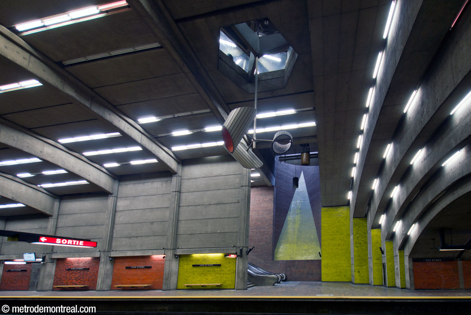 A view of the main volume from the Montmorency platform, showing how the vaults (left) are repeated by shallower vaults on the eastern wall of the volume (right). In the background, over the foot of the escalators to the opposite platform, a tall triangular light shaft is emphasized by yellow glazed bricks. Jacques de Tonnancour's sculpture is overhead.