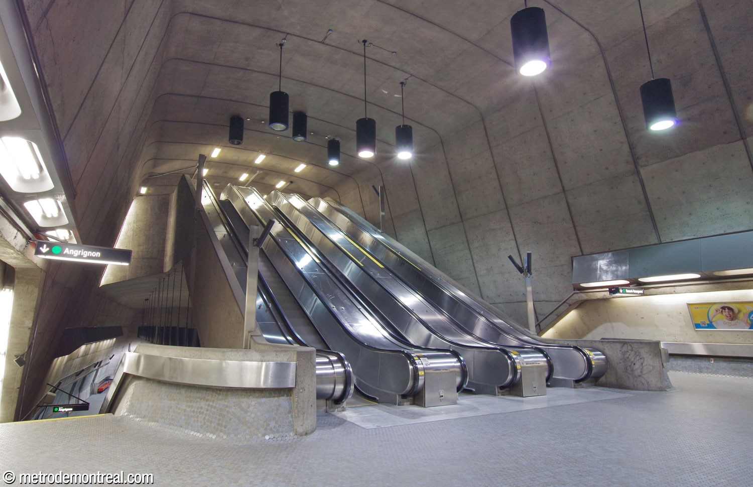 Vue oblique de la volée centrale d’escaliers mécaniques. On en aperçoit la forme monolithique monumentale en béton.