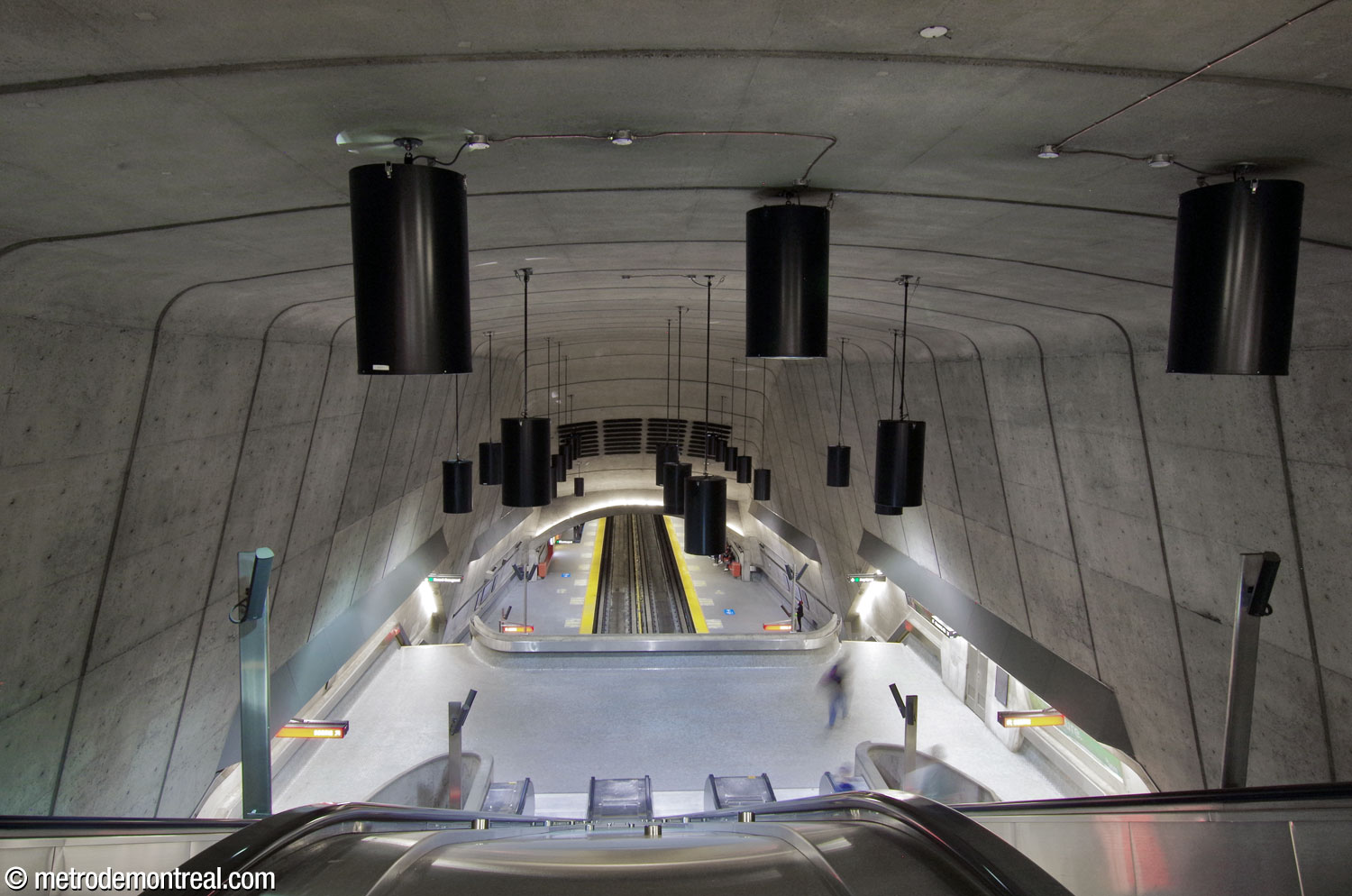 Une autre vue depuis la tête des escaliers mécaniques, le long du grand volume. On remarque la « fenêtre » ronde constituée du parapet de la passerelle, des murs du volume et de la voûte de la nef.