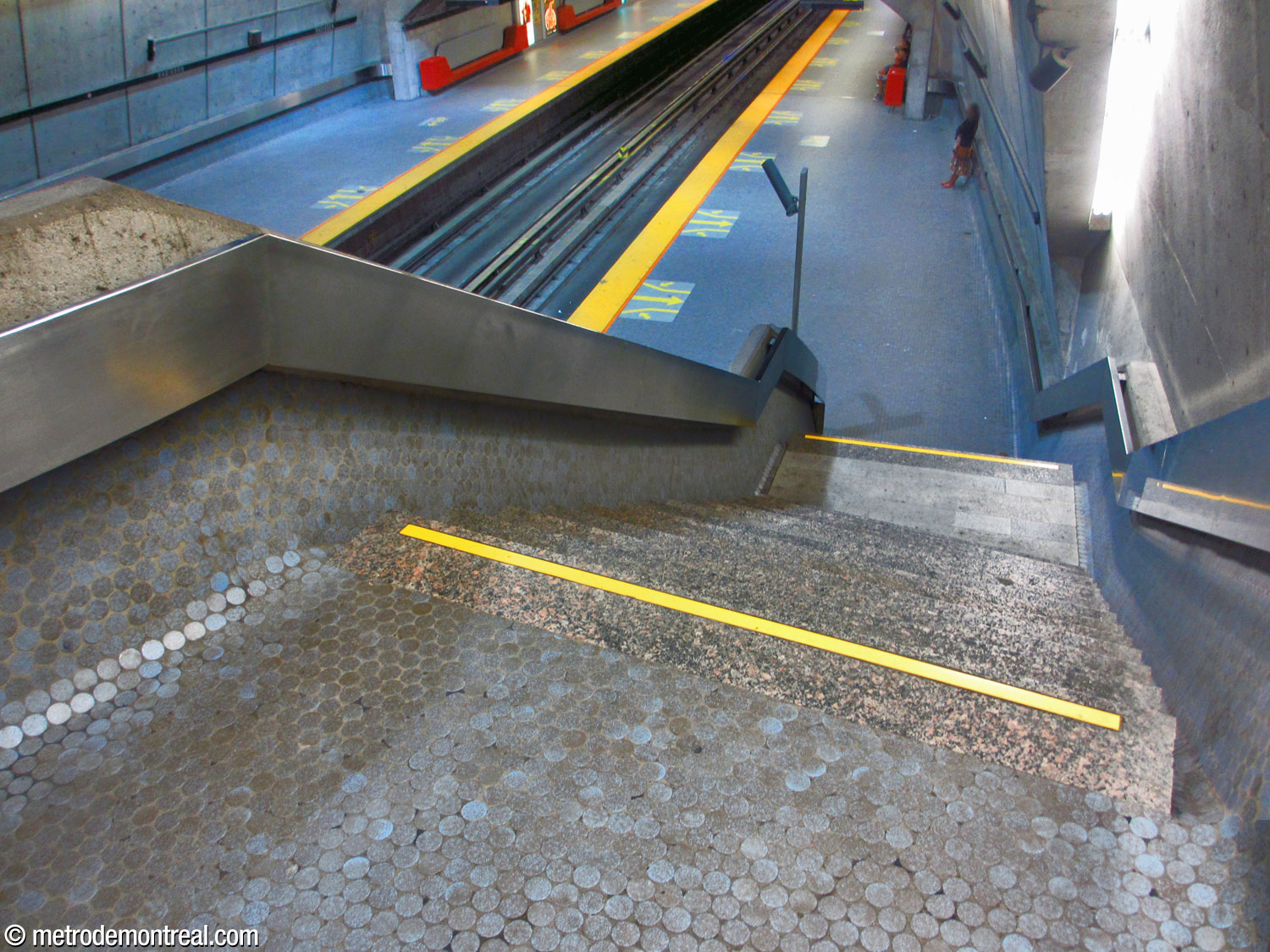 L'un des escaliers reliant la passerelle au quai Angrignon. On remarque la courbe de l’escalier qui épouse la forme en fuseau du mur du grand volume, ainsi que les coins arrondis au pied du mur et du parapet.
