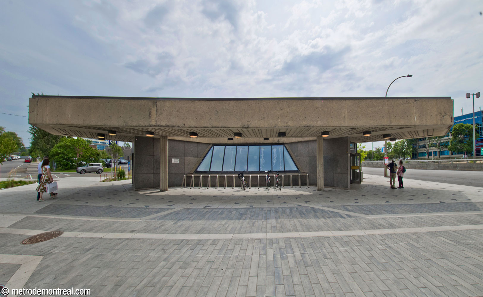 Panorama de la façade nord-ouest de l'édicule. Cette façade est abritée par une longue et profonde saillie du toit. Les deux entrées se trouvent de part et d’autre de cette façade, derrière les coins du bâtiment. Une ouverture dans la saillie illumine la large fenêtre au centre.
