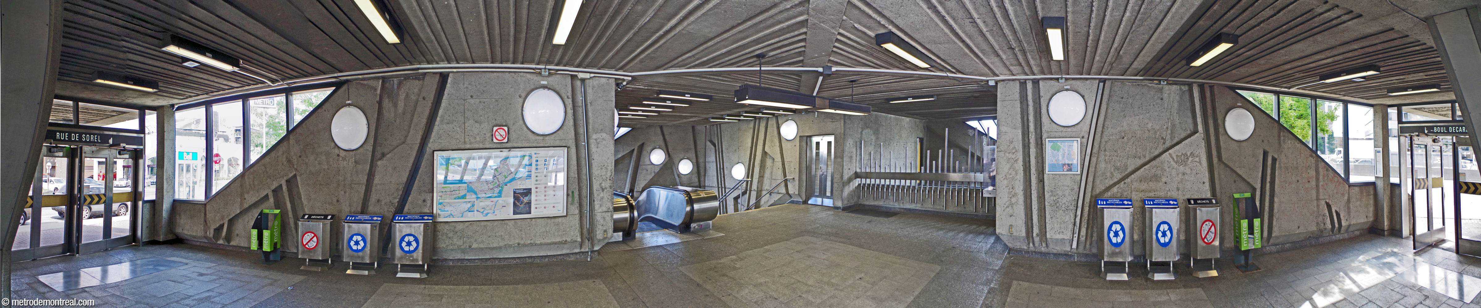 Panorama de l'intérieur de l'édicule. De gauche à droite : l'entrée de la rue de Sorel; l'escalier vers la billetterie; le puits de lumière; l'entrée du boulevard Décarie. Les murs partagent les bas-reliefs anguleux et les luminaires hémisphériques de la salle de contrôle.