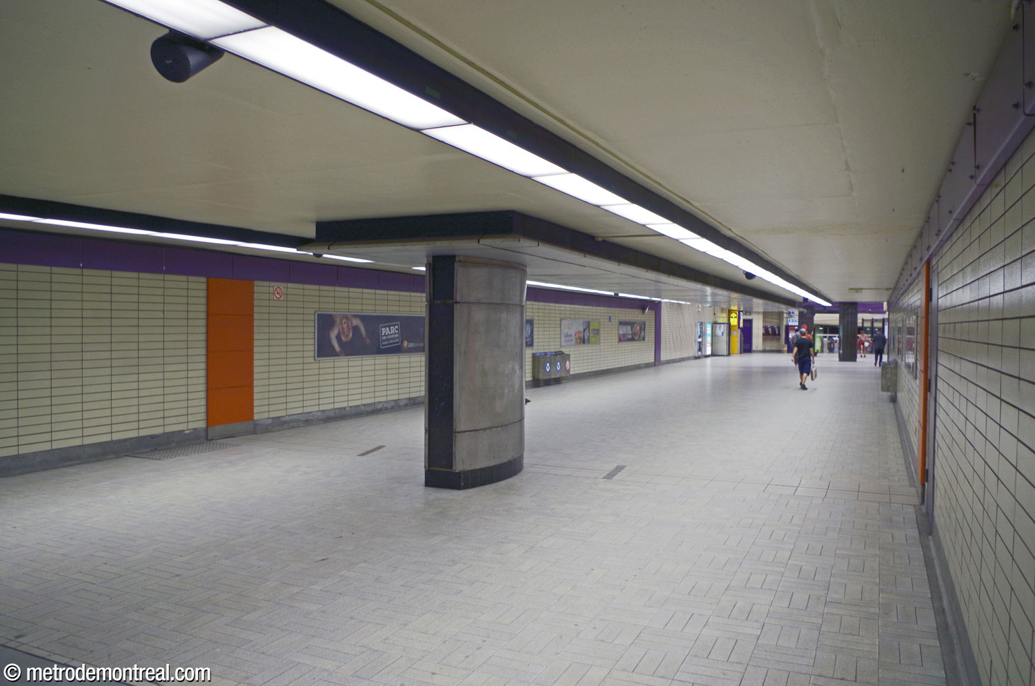 The hallway from the Berri Ouest entrance to the ticket hall. The orange and purple accents amid the straw-coloured walls unify it with the rest of the station's interior. The metal housing in the middle of the hall was a unique solution to the need to add utility conduits in the early 2000s.