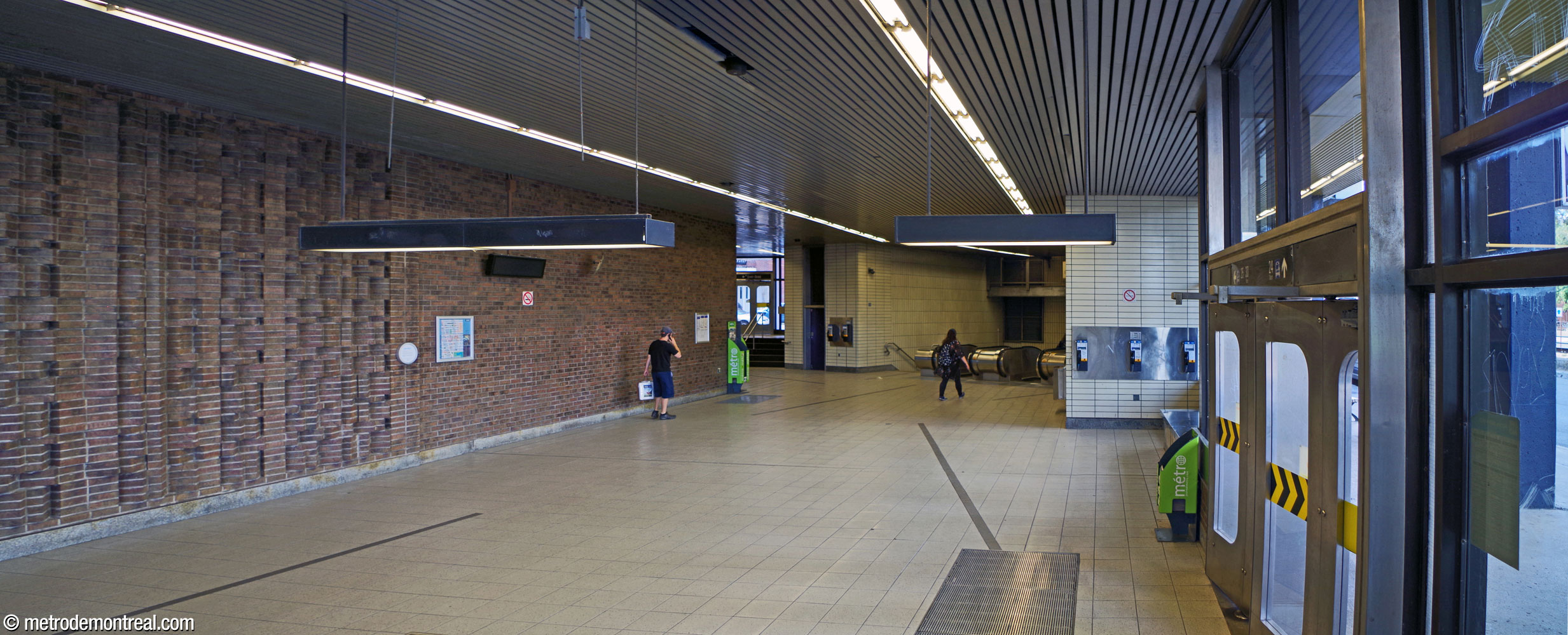 The long, spacious interior of the Berri Ouest entrance. The exit onto Rue de Rigaud is behind the viewer, with Rue Berri on the right. At the end of the space is the stairwell leading down to the station, and next to it, stairs up to the Rue de Malines exit. The left wall of the room hosts Mario Merola's brickwork relief Rivières.