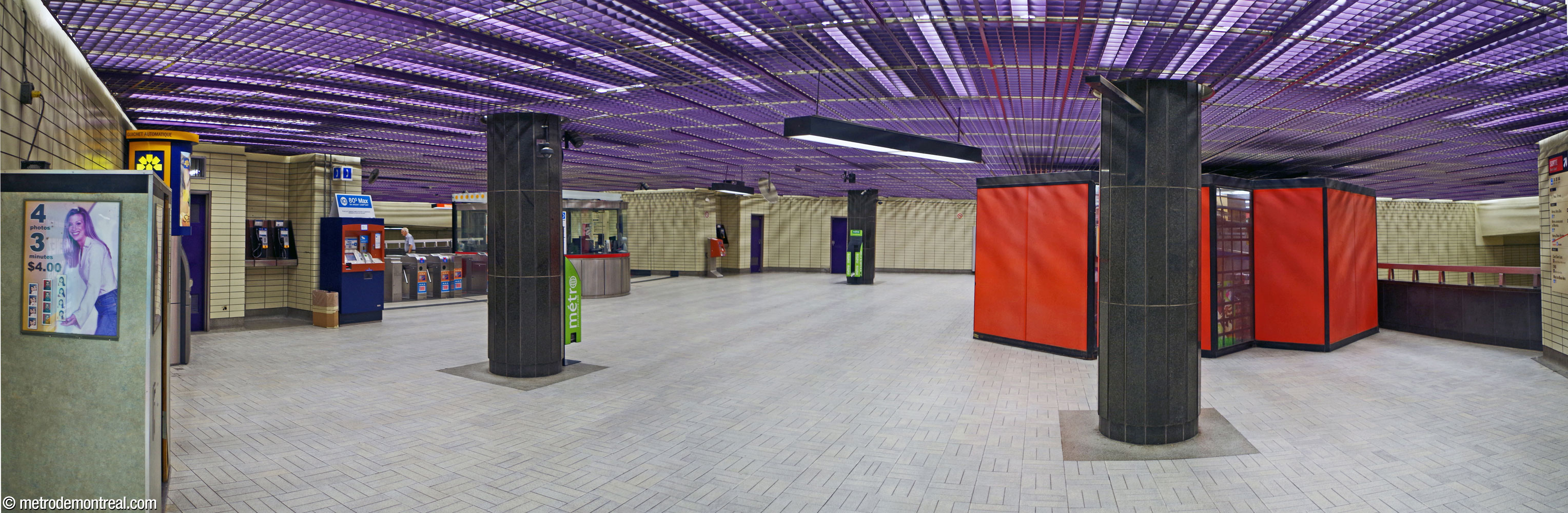 The concourse of the ticket hall level, where the corridors from the two accesses converge. The gateline is at left; at right is a parapet overlooking the south end of the platforms. At centre is a concession walled with orange panels. The hallway toward the Berri Ouest exit is beyond the right edge of the frame.
