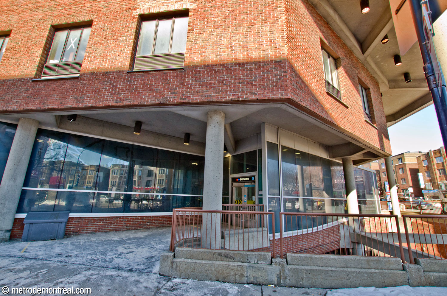 The entrances to the headhouse are located at either end of an enclosed walkway under the building’s overhang, alongside the sunken garden. The entrance visible here, leading to Avenue de Westbury on the west side of the building, is reached via a ramp.