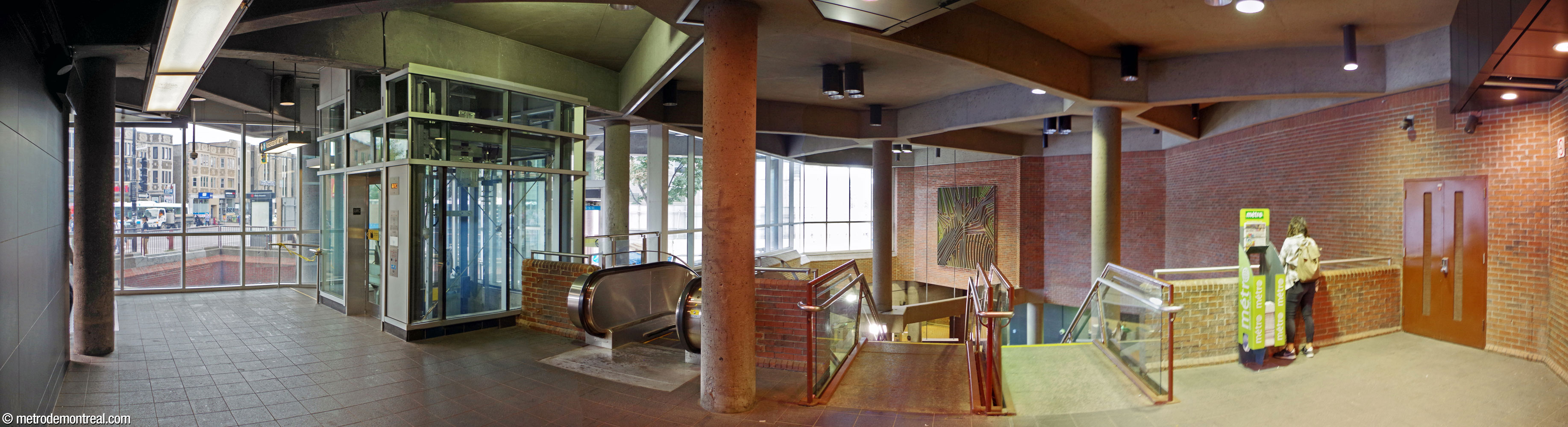 Panorama of the landing inside the entrance to the headhouse. The two entrance doors, opening onto Chemin Queen-Mary and Avenue de Westbury, are at either end of a diagonal walkway passing by the elevator (left). The relatively shallow landing then opens onto a wide overlook over the ticket hall, to which it connects by two staircases and an upward escalator.