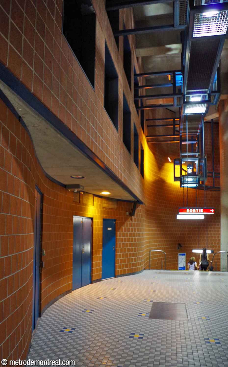 The undulating wall along the landing above the departure platform, at the foot of the stairs to the ticket hall. Above, a grid of dark square openings conceals a ventilation shaft.