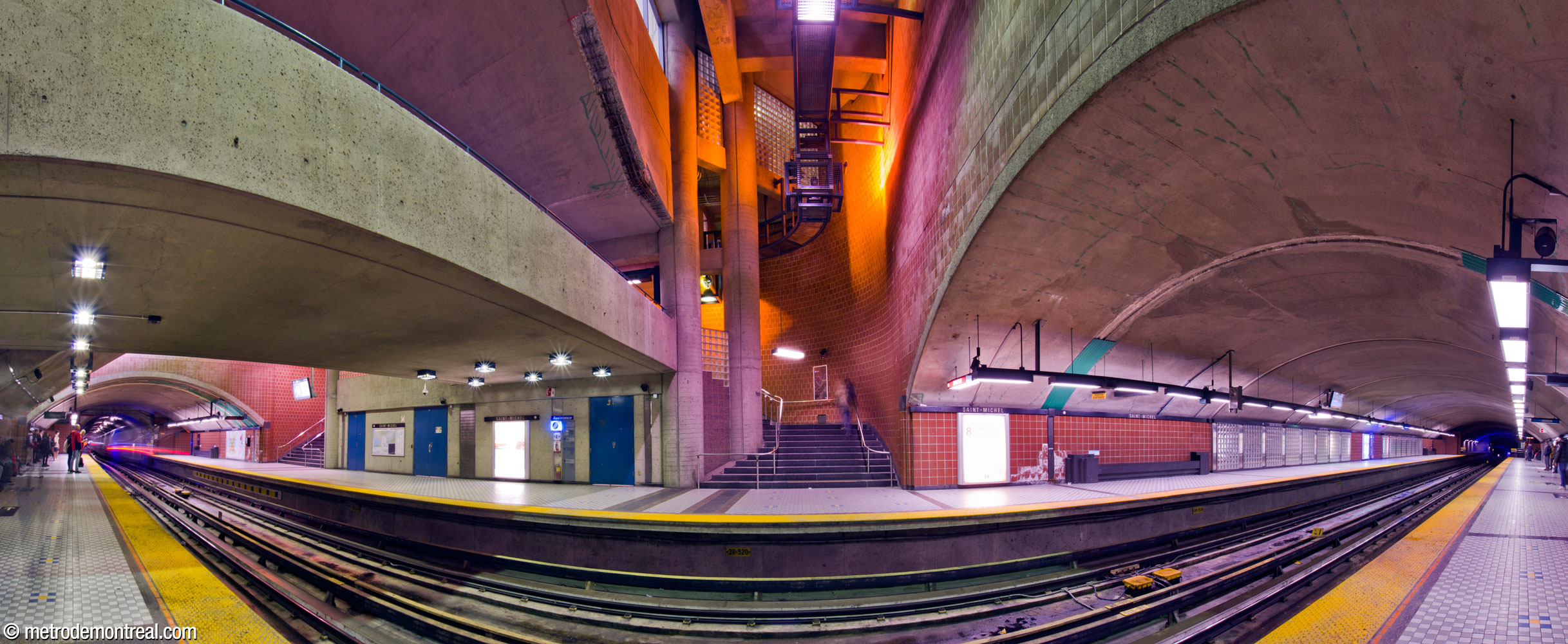 The trainroom of Saint-Michel station, seen from the departure platform within the central volume. The edge of the crossover (left) and the spandrel wall above the trainroom vault (right) define a high vertical space housing stairs up to the transept level (centre). Walls are clad in square terra cotta blocks, with glass block accents; the glass block panels covering the station's artworks are at right.