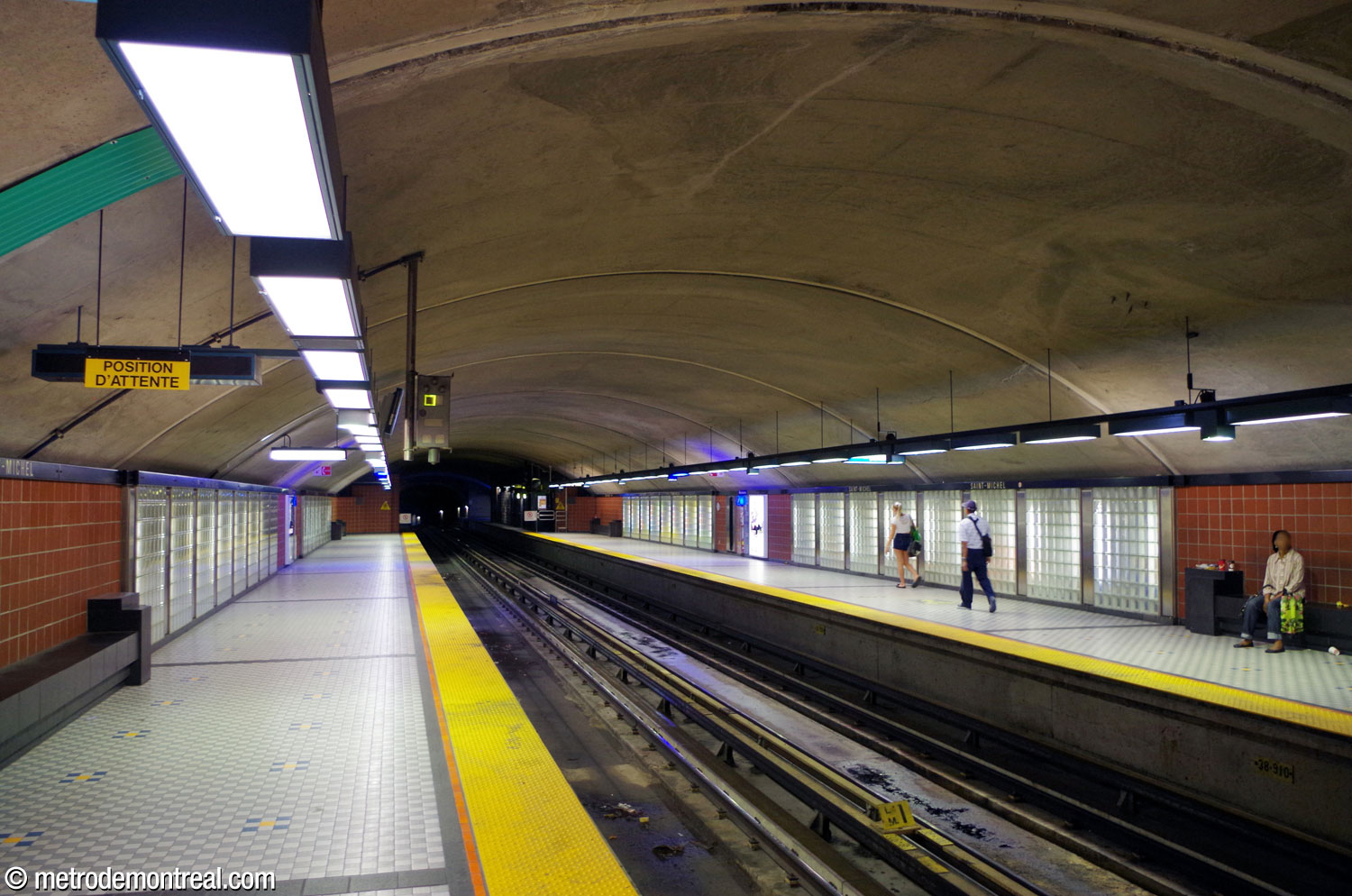 Looking toward the western end of the platforms from the arrival (Saint-Michel) platform. The four panels of glass blocks enclose the station's artworks; the bright colours of Marcelin Cardinal's mural can be glimpsed in the centre-right display.