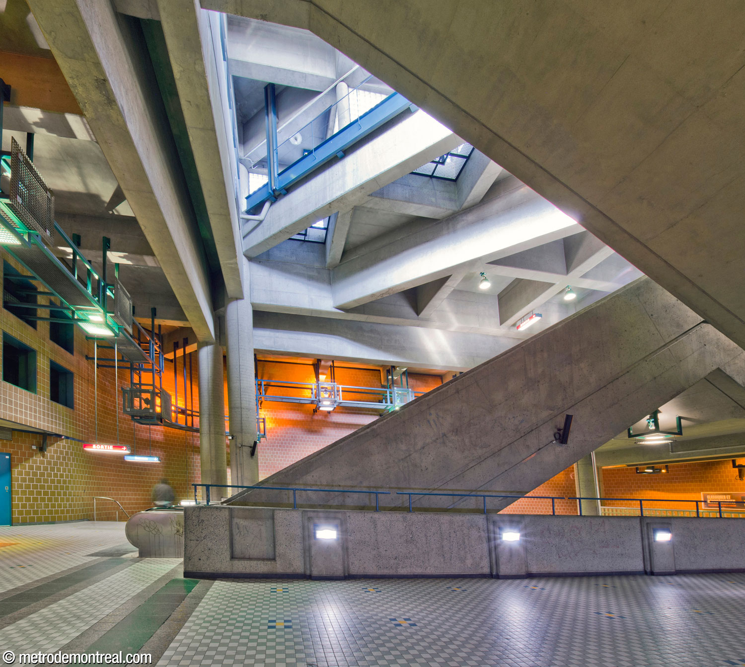 The stairwell from the transept level to the ticket hall, seen from its west side, rises through the main volume. At left, the landing at its foot leads to the departure platform; in the foreground is the crossover from the arrival platform. Overhead, windows and skylights in the east headhouse admit natural light.