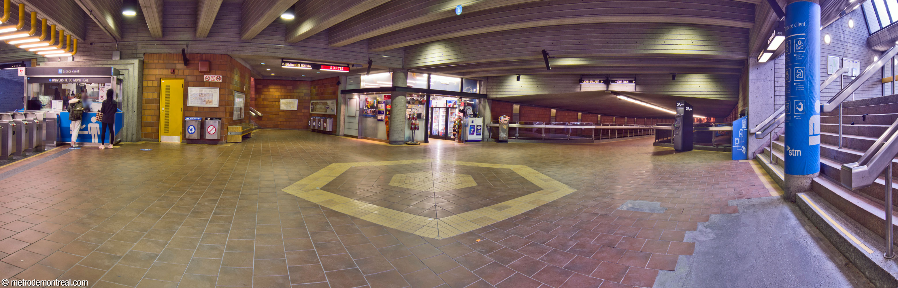 Panorama du niveau mezzanine, montrant sa connexion aux trois accès de la station. À droite, l'accès principal. Au centre, une passerelle parcourt la pleine longueur de la nef de la station au-dessus des voies pour atteindre l'accès Louis-Colin. Au centre gauche, entre la loge et le commerce, l'escalier vers la sortie Université de Montréal. La loge et la barrière de perception sont à gauche.