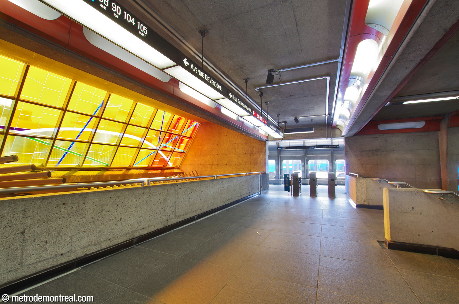 View along the bridge, looking toward the south access. When the stairs between the bridge and ticket hall were built, exit-only turnstiles were added on both ends of the bridge; as a result, passengers could not enter the metro via the south side of the headhouse. At some point before summer 2025, the ones on the south end were replaced by entrance turnstiles, to restore access from the south side. Marcelle Ferron’s stained glass window and sculpture are at left.