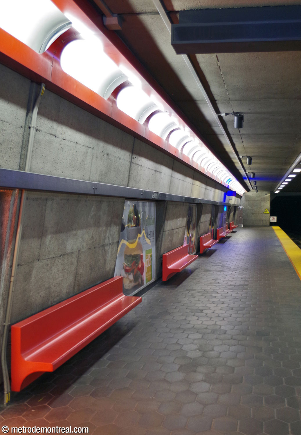 The lightly tilted walls of the platforms, with their red-orange seats and light fixture housings standing out from the bare concrete.