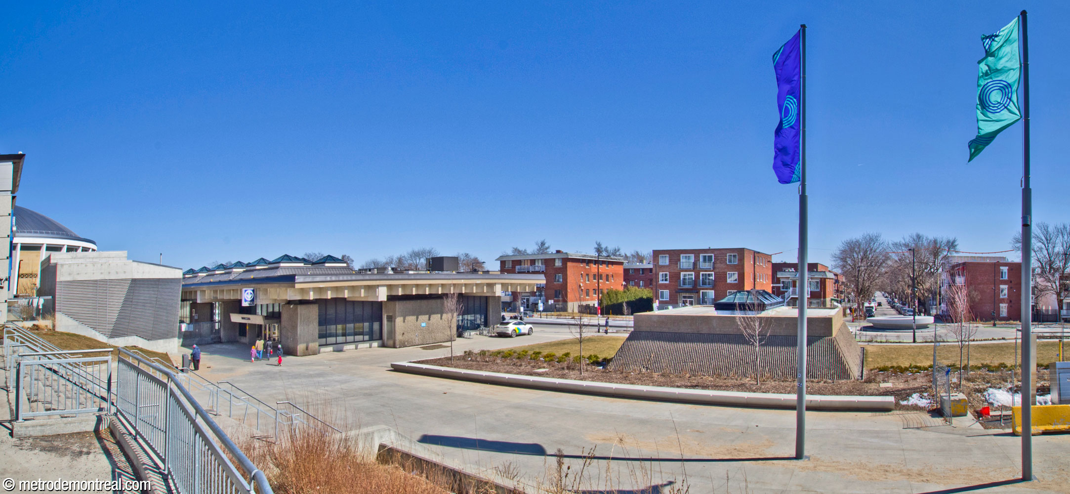 Exterior view of the north and west sides of the headhouse and bus loop, seen from the Olympic Park. The skylights on the roof are visible, as is the head of the light and ventilation shaft serving the trainroom. The large, striped concrete cube at left is the headhouse for the Viau attachment centre, located just north of the station.