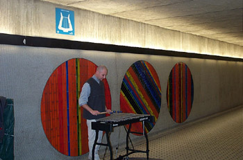 A busker playing the xylophone in Peel metro. Note the blue lyre symbol indicating a designated area for musicians.