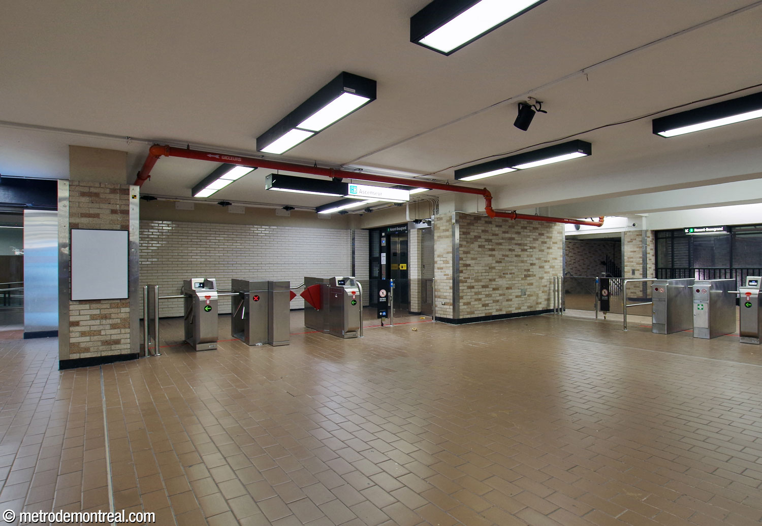 The separate fare-paid zone for the elevator to the Honoré-Beaugrand platform occupies an alcove walled in white brick (left), in the southwest corner of the concourse.