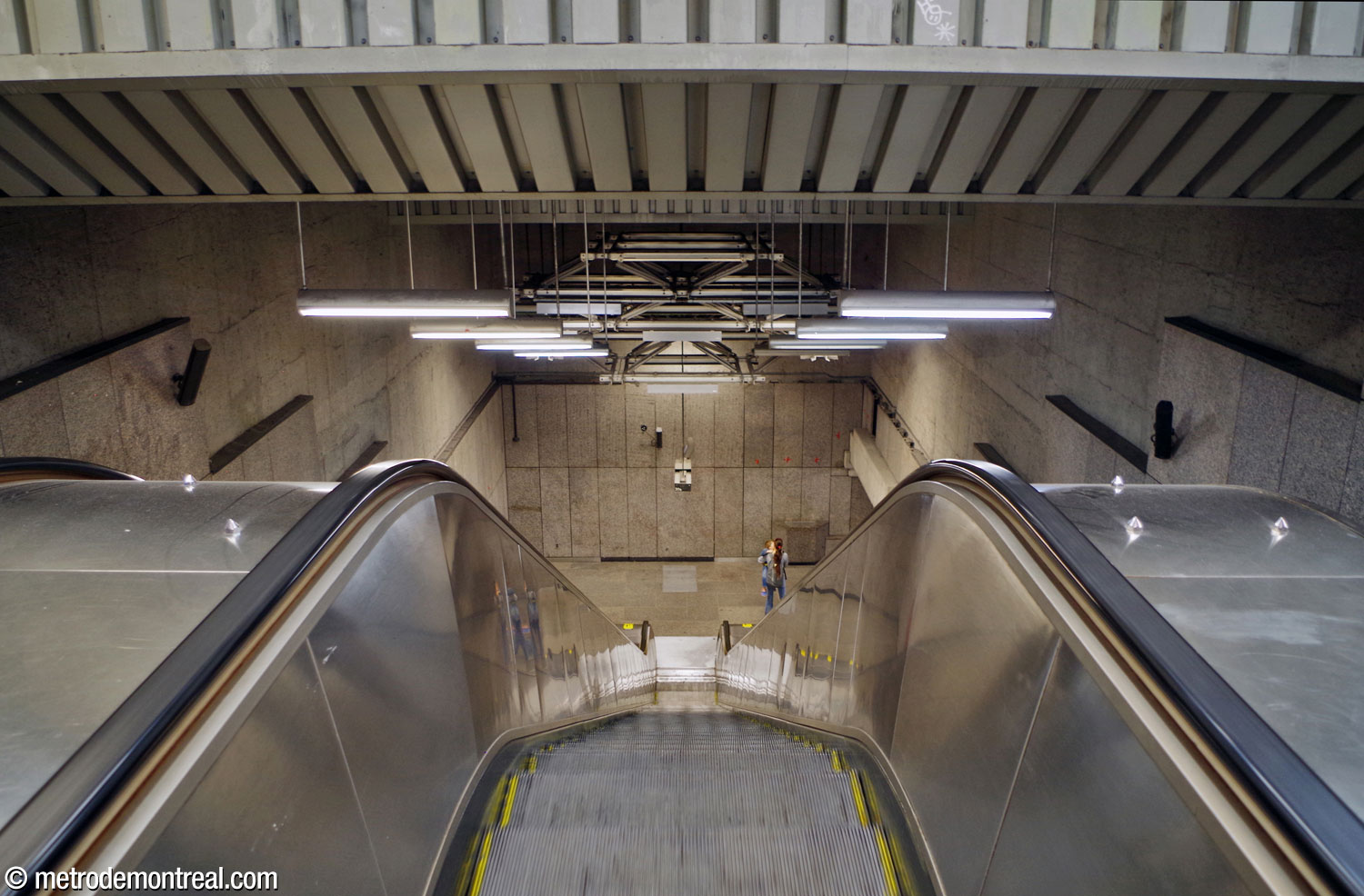The deep volume of the stairwell down from the landing of the Côte-des-Neiges Est entrance, with a section of the station's spaceframe overhead.