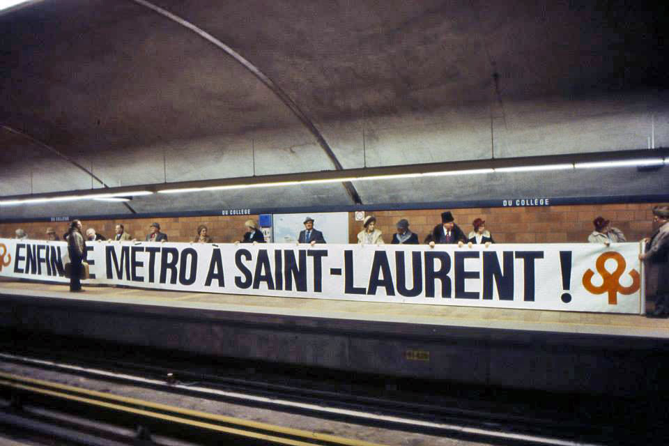 Des personnages en costumes d'époque tiennent une bannière commémorant l'arrivée du métro à Ville Saint-Laurent lors de l'inauguration de la station le 9 janvier 1984.