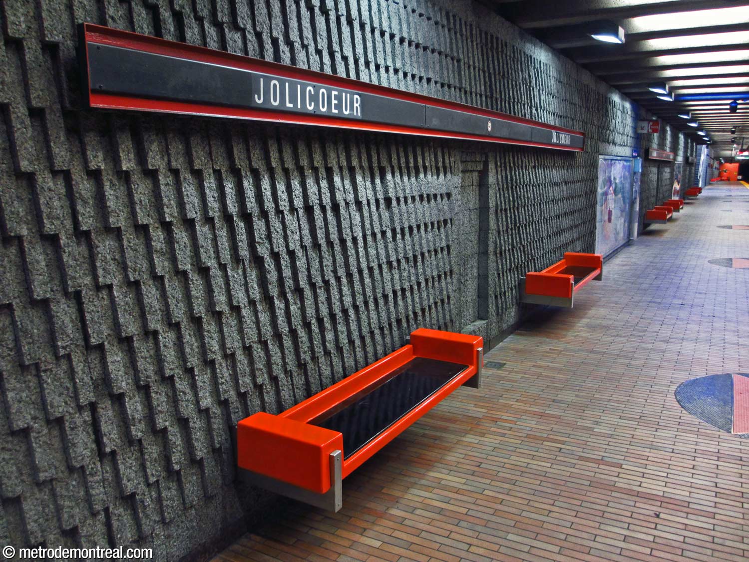 Le briquetage vertical des murs des quais, les bancs rouge-orange et noir, et les bandeaux de nom encadrés de rouge-orange.