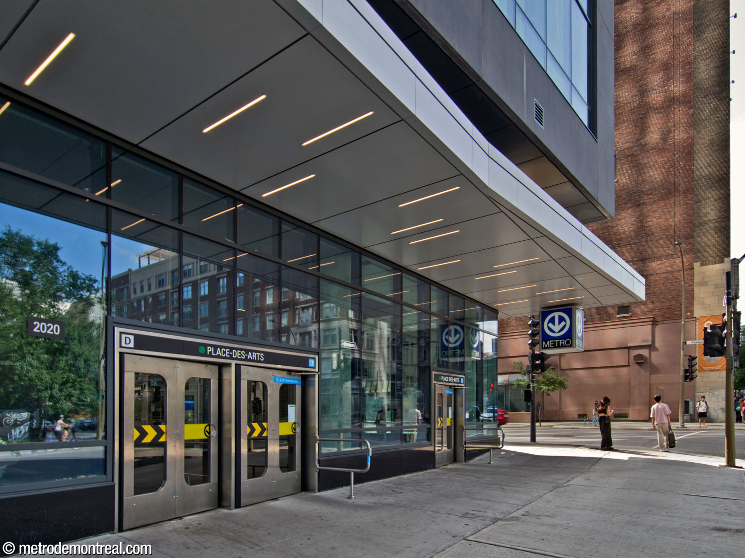 Closer view of the glass curtain wall of the De Bleury Nord entrance under the building’s overhang. Note the unusual cube-shaped metro sign.