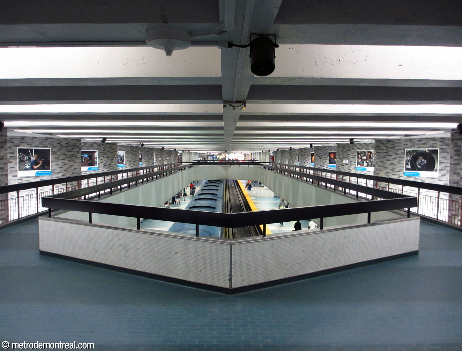 The walkways above the platforms, connecting the east and west ticket halls, seen here facing east. The twinned walkways are separated by a long opening overlooking the platforms below, with crossovers on either end of it. Various exhibits are displayed on the wall zigzags.