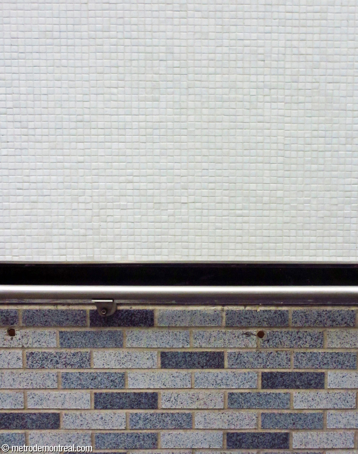 The station's main finishes: varying shades of light and dark speckled blue-grey glazed brick, and small, square white tiles.