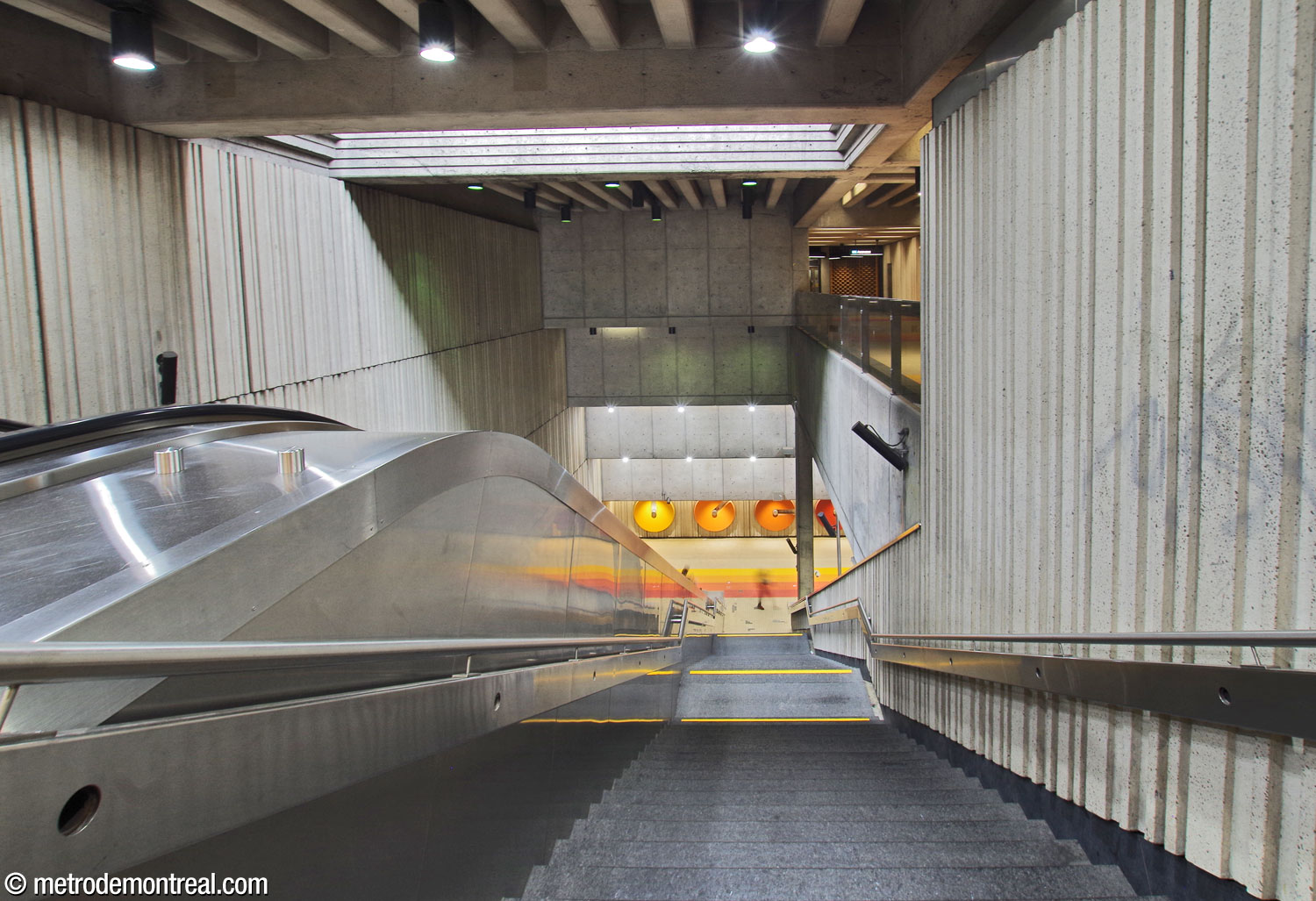 Le volume au-dessus de l'escalier principal entre la billetterie et le transept. En haut, un puits de lumière fournit un éclairage naturel. En haut à gauche, on voit le corridor entre l’ascenseur supérieur et la billetterie, qui donne sur le volume. La deuxième suite de sculptures murales d'André Léonard orne le mur en face du pied des escaliers.